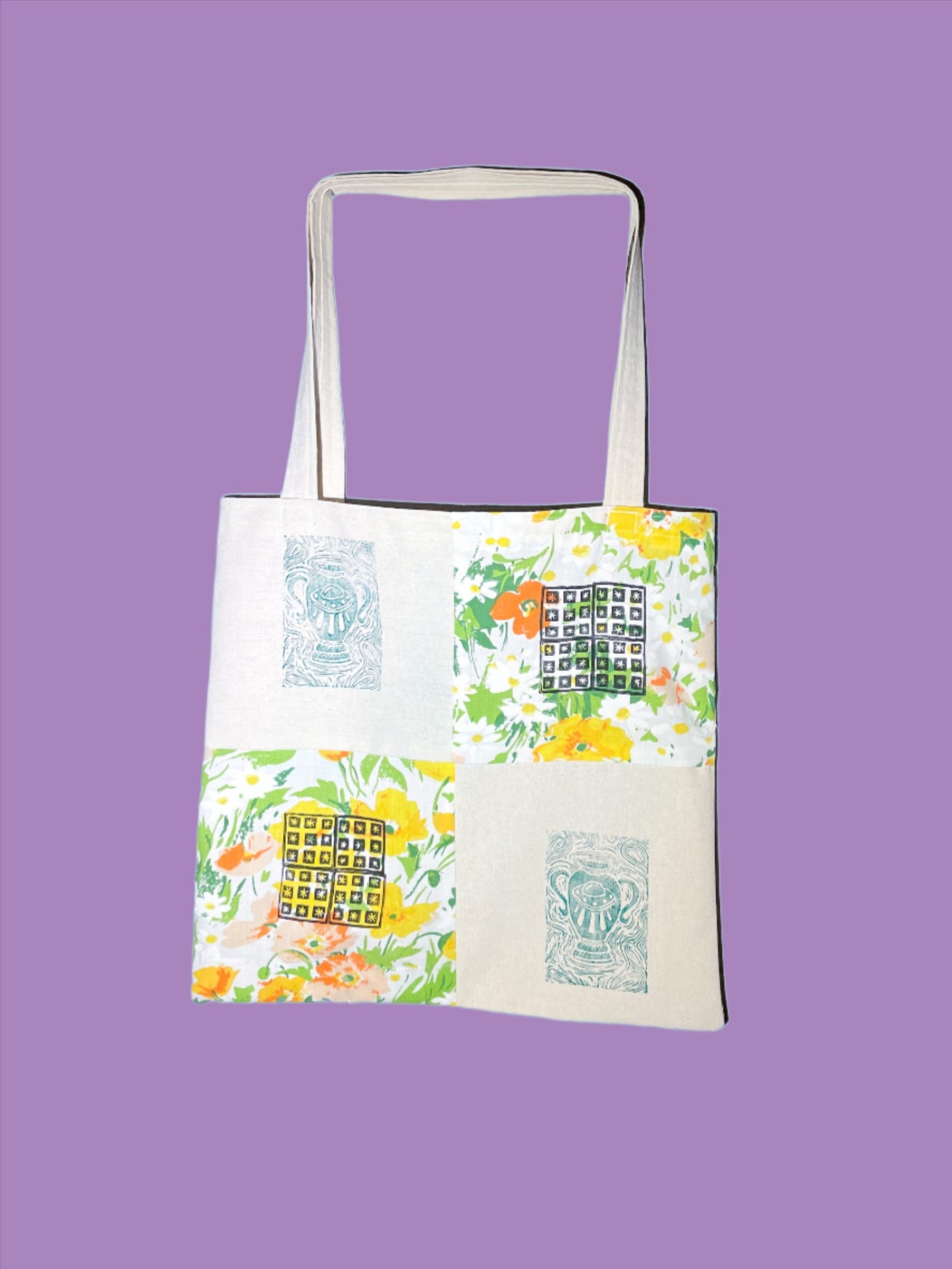quilted canvas tote bag sits against a tiffany blue backdrop. the bag is quilted in four simple squares, with a thrifted floral fabric in orange and green. On each square is a block printed image in green or red, the canvas squares have a green UFO amphora vase and the floral squares have a small quilted floral block print design on them. 
