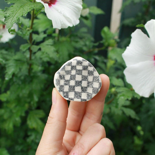 tiny checkered bud vase held in hand against dark foliage with hibiscus flowers.